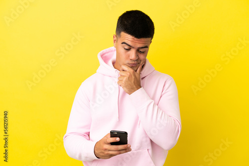 Young handsome man over isolated yellow background thinking and sending a message