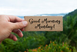 Hand holding wooden banner with Good Morning Monday text. With beautiful nature background. Morning wishes concept.