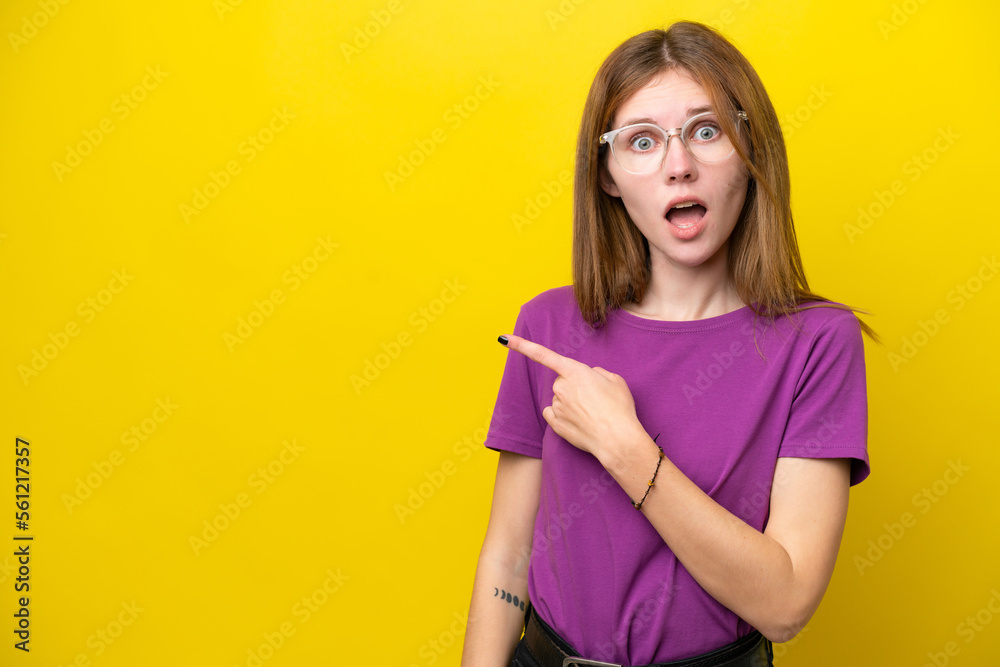 Young English woman isolated on yellow background surprised and pointing side
