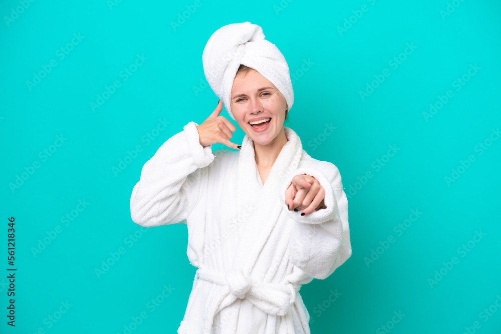 Young woman in a bathrobe isolated on blue background making phone gesture and pointing front Young woman in a bathrobe isolated on blue background making phone gesture and pointing front
