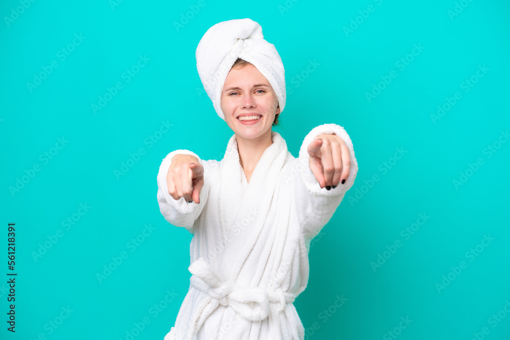 Young woman in a bathrobe isolated on blue background points finger at you while smiling Young woman in a bathrobe isolated on blue background points finger at you while smiling