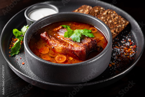 Solyanka soup with meat, sausage, vegetables, olives and lemon in bowl on wooden table background