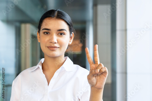 Happy smiling young south asian Indian woman pointing up 2 fingers, showing V for victory, number two, second place or 2 points gesture, photo