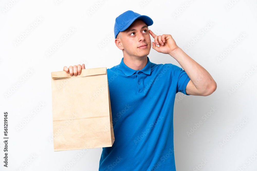 Young Brazilian man taking a bag of takeaway food isolated on white background having doubts and thinking Young Brazilian man taking a bag of takeaway food isolated on white background having doubts and thinking