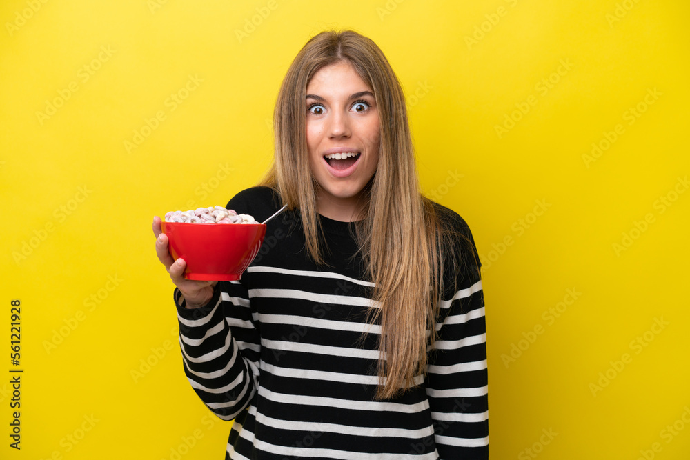 Young caucasian woman holding a bowl of cereals isolated on yellow background with surprise and shocked facial expression Young caucasian woman holding a bowl of cereals isolated on yellow background with surprise and shocked facial expression