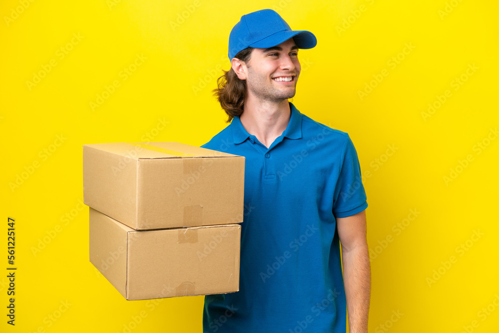 Delivery handsome man isolated on yellow background looking to the side and smiling Delivery handsome man isolated on yellow background looking to the side and smiling