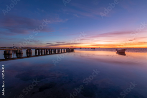 Beautiful seascape at sunrise in the Mar Menor, Los Alcazares, Spain. With a spectacular sky, very colorful and reflected in the calm waters of the sea. We also see a wooden jetty and boats on the wat