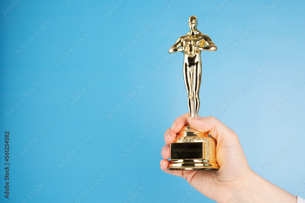 Oscar statue, award in hand on blue background,copy space - obrazy, fototapety, plakaty 