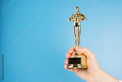 Fotografie, Obraz Oscar statue, award in hand on blue background,copy space