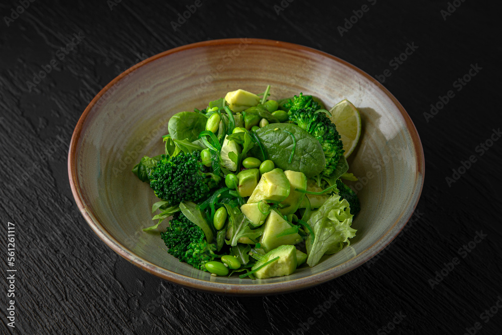Green Salad from avocado, beans, broccoli in a ceramic plate on a dark textured background. Restaurant menu Isolated on black Green Salad from avocado, beans, broccoli in a ceramic plate on a dark textured background. Restaurant menu Isolated on black