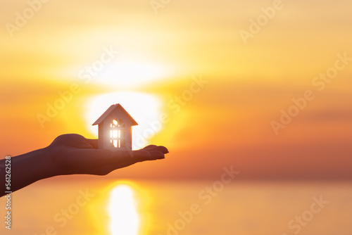 real estate purchase sale and rent, hand holding a house against the background of a sea sunset