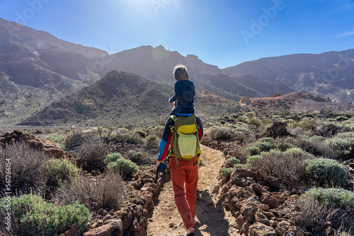 Aktiv auf Teneriffa, Kanarische Inseln: Wanderung im Teide Gebiet zum dritthöchsten Gipfel Alto de Guajara - Mann mit Kind auf dem Rücken wandert in der Sonne photo