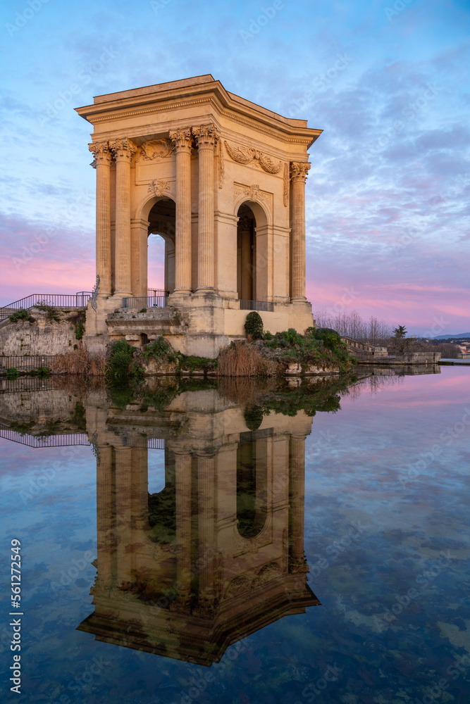 Colorful winter view before sunrise of ancient water tower stone building with reflection in water pool in landmark Promenade du Peyrou garden, Montpellier, France