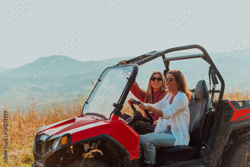 Two young happy excited women enjoying beautiful sunny day while driving a off road buggy car on mountain nature