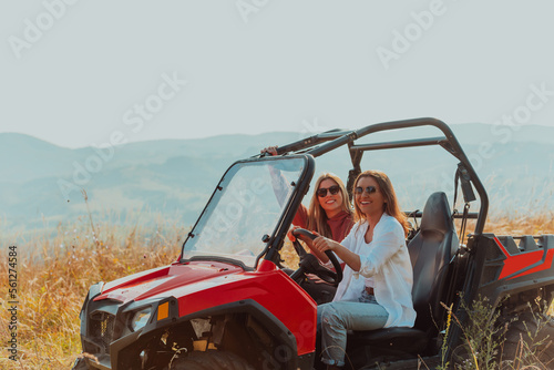 Two young happy excited women enjoying beautiful sunny day while driving a off road buggy car on mountain nature