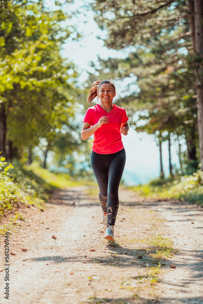 Young happy woman enjoying in a healthy lifestyle while jogging on a country road through the beautiful sunny forest, exercise and fitness concept Young happy woman enjoying in a healthy lifestyle while jogging on a country road through the beautiful sunny forest, exercise and fitness concept