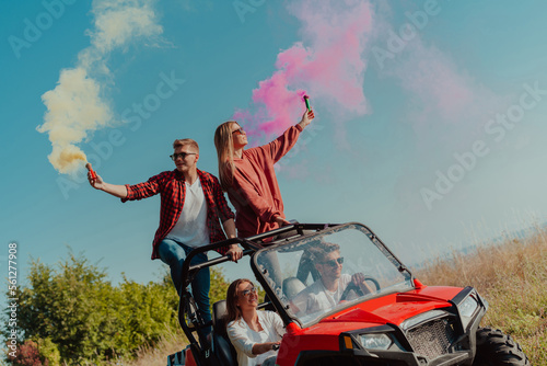 Group of young happy excited people having fun enjoying beautiful sunny day holding colorful torches while driving a off road buggy car on mountain nature. 