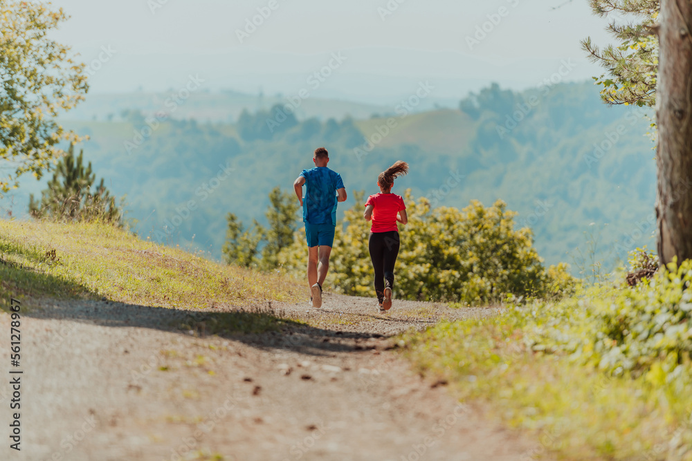 Couple enjoying in a healthy lifestyle while jogging on a country road through the beautiful sunny forest, exercise and fitness concept