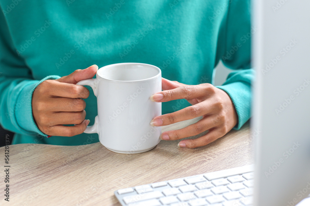 Hand of woman wearing tosca sweater holding white mug for mock up at office desk Hand of woman wearing tosca sweater holding white mug for mock up at office desk