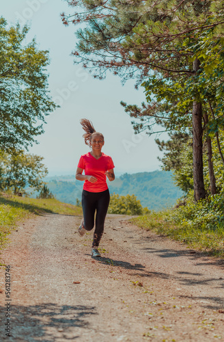Fototapeta Naklejka Na Ścianę i Meble -  Young happy woman enjoying in a healthy lifestyle while jogging on a country road through the beautiful sunny forest, exercise and fitness concept