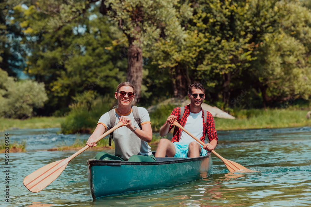 Couple adventurous explorer friends are canoeing in a wild river surrounded by the beautiful nature