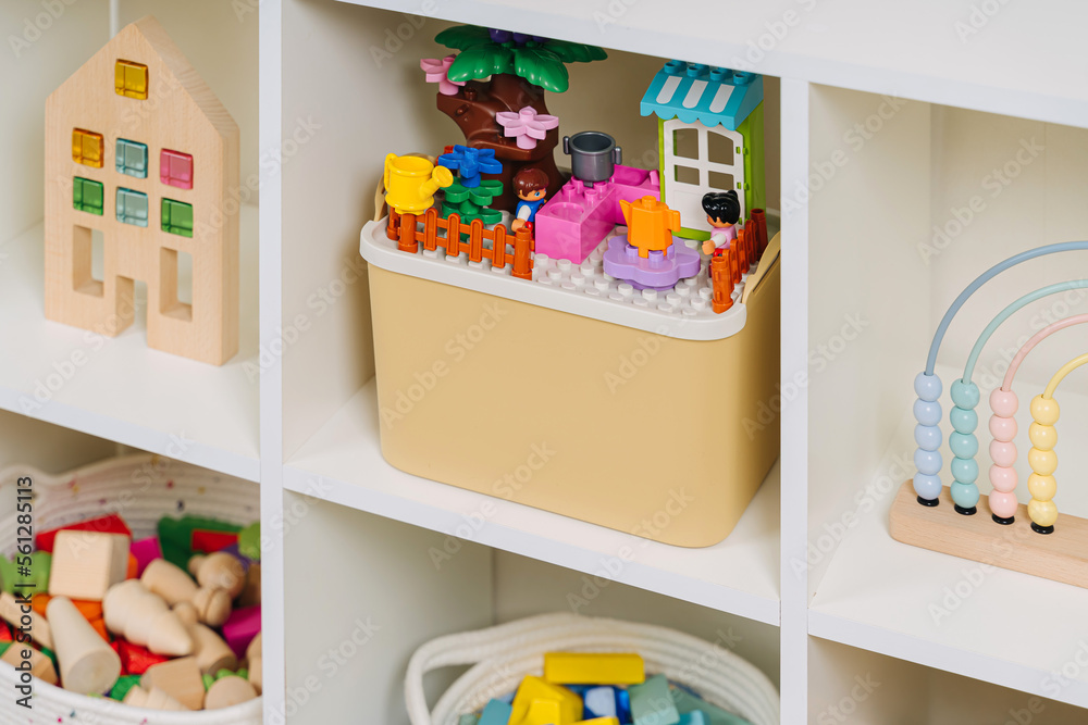 Naklejka premium White shelving with rainbow wooden toys and constructor pieces in storage baskets and boxes. Organizing and storage ideas in nursery.
