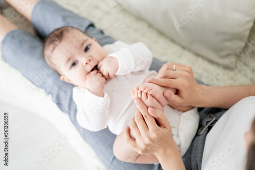 mom s hands hold the little nights of a newborn baby on a white sofa. Maternal love and care. Baby s heels in focus