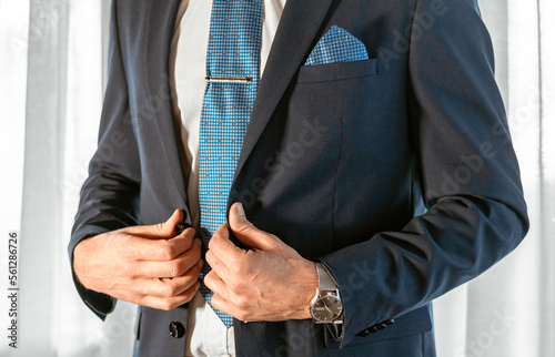 Man in blue tuxedo correct his buttons on his jacket. Wedding details. You can see the sky blue pocket square, the tie clip and the watch on his wrist.