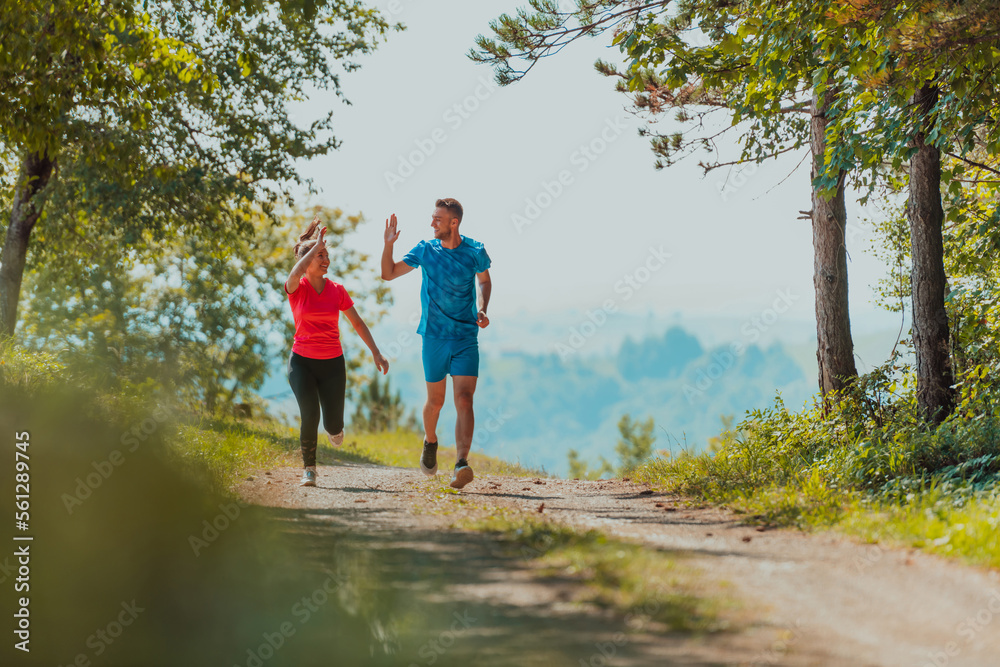 Couple enjoying in a healthy lifestyle while jogging on a country road through the beautiful sunny forest, exercise and fitness concept