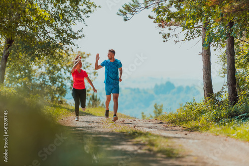 Couple enjoying in a healthy lifestyle while jogging on a country road through the beautiful sunny forest, exercise and fitness concept © .shock