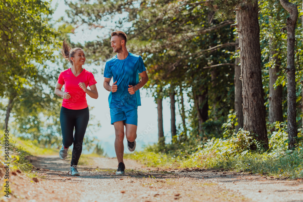 Fototapeta premium Couple enjoying in a healthy lifestyle while jogging on a country road through the beautiful sunny forest, exercise and fitness concept