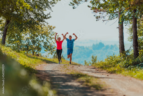 Couple enjoying in a healthy lifestyle while jogging on a country road through the beautiful sunny forest, exercise and fitness concept © .shock