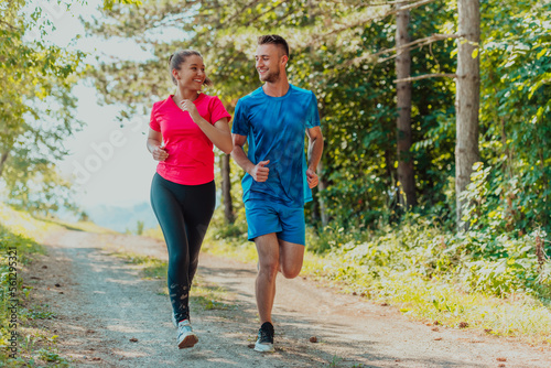 Fototapeta Naklejka Na Ścianę i Meble -  Couple enjoying in a healthy lifestyle while jogging on a country road through the beautiful sunny forest, exercise and fitness concept