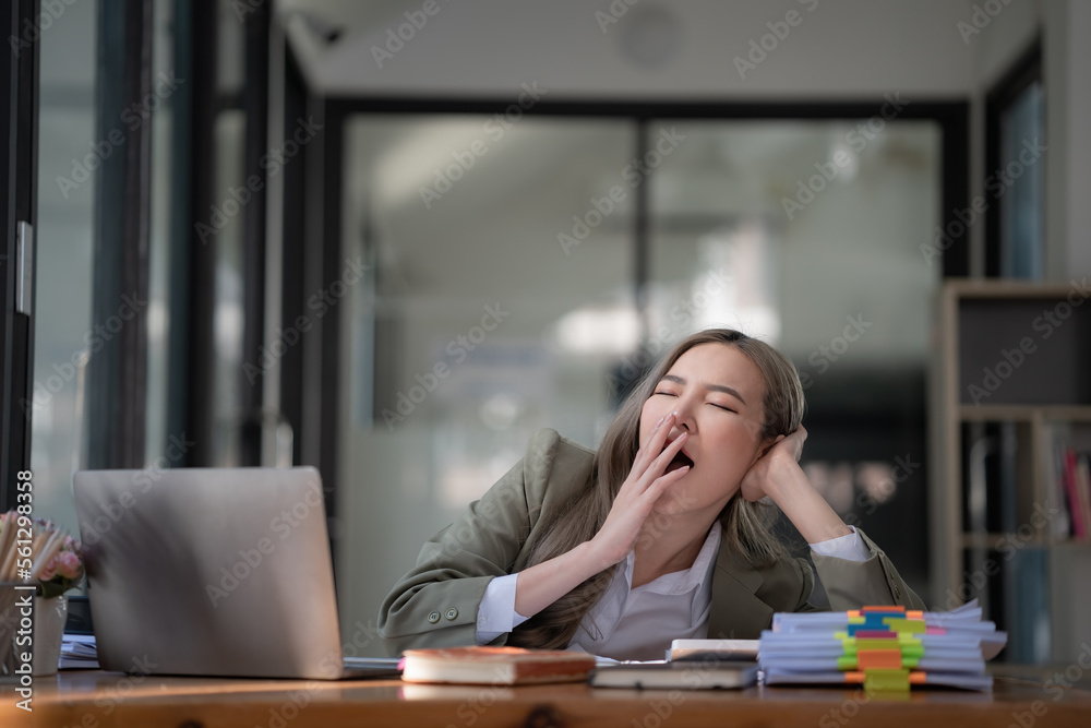 Young Asian businesswoman yawning while working with a laptop computer at the office, a woman in casual office lifestyle concept. Young Asian businesswoman yawning while working with a laptop computer at the office, a woman in casual office lifestyle concept.