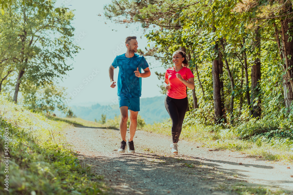 Couple enjoying in a healthy lifestyle while jogging on a country road through the beautiful sunny forest, exercise and fitness concept Couple enjoying in a healthy lifestyle while jogging on a country road through the beautiful sunny forest, exercise and fitness concept