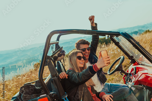 Young happy excited couple enjoying beautiful sunny day taking selfie picture while driving a off road buggy car on mountain nature