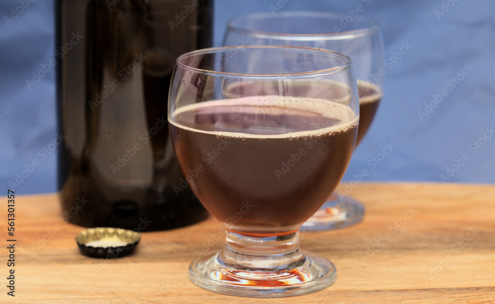 Still life with dark brown craft beer bottle on a wooden board against dark blue background Still life with dark brown craft beer bottle on a wooden board against dark blue background