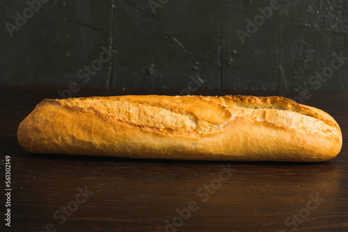 Appetizing french baguette with crust on dark wooden table, background with space for text
