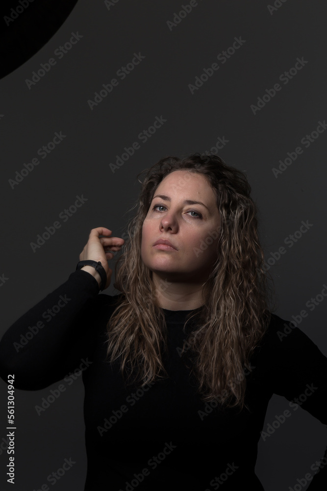 a woman with curly hair on a dark background, a woman over 30 years old showing negative emotions, a portrait of a tense face in dark clothes a woman with curly hair on a dark background, a woman over 30 years old showing negative emotions, a portrait of a tense face in dark clothes