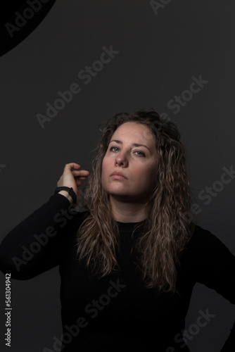 a woman with curly hair on a dark background, a woman over 30 years old showing negative emotions, a portrait of a tense face in dark clothes