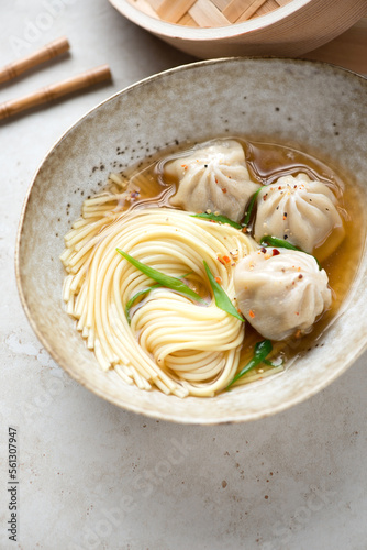 Bowl of asian noodle soup with wontons on a beige stone background, vertical shot, middle close-up, selective focus