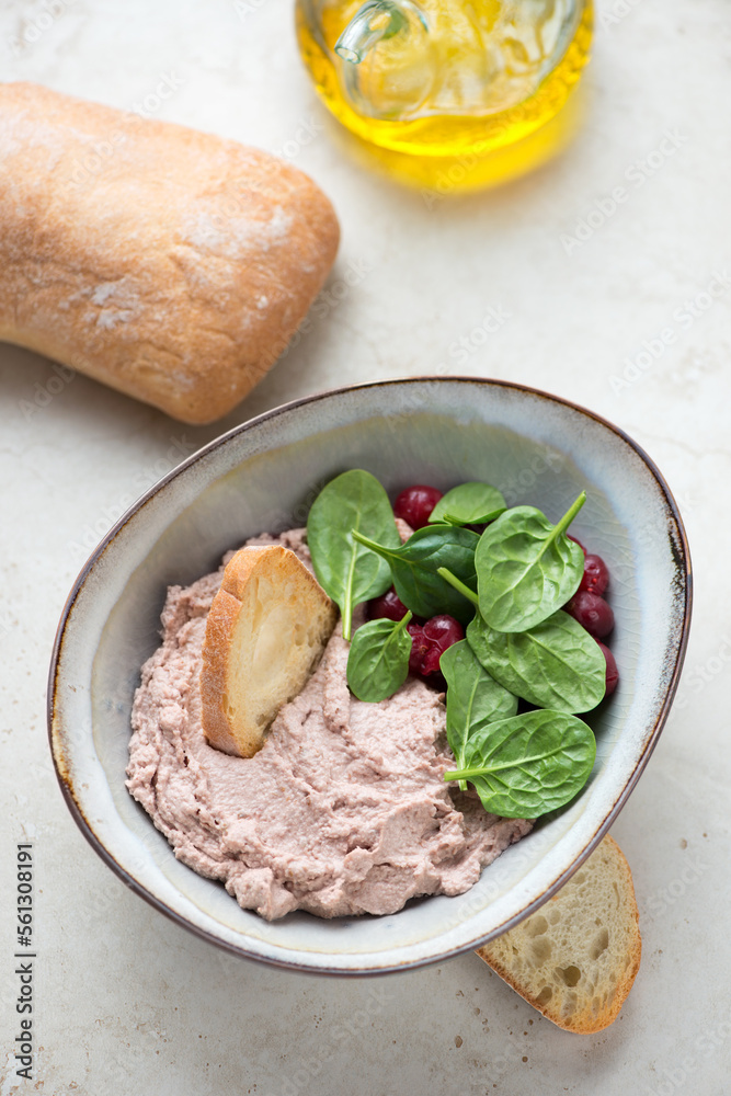 Bowl of liver pate with cranberry sauce, fresh spinach and ciabatta, vertical shot on a beige stone background