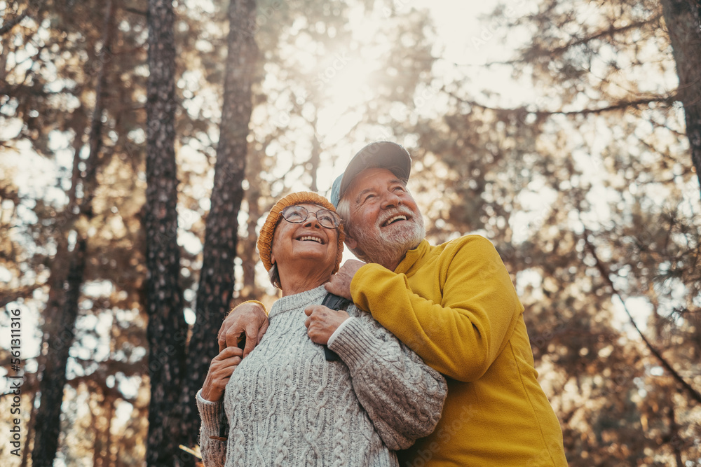 Head shot portrait close up of middle age cheerful people smiling and looking at the the trees of the forest around them. Active couple of old seniors hiking and walking together in the mountain 