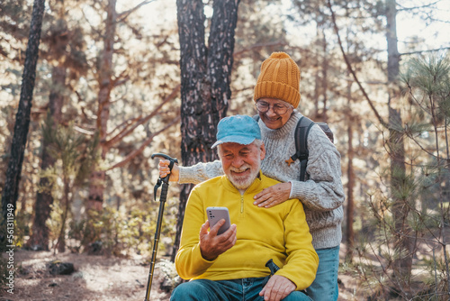 Head shot portrait close up of couple of cute seniors using phone together in the forest with trees around them. Using cellphone mobile outdoors having fun and enjoying. © Daniel