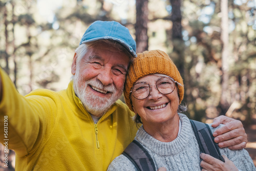 Obraz na plátně Head shot portrait close up of cute couple of old seniors taking a selfie together in the mountain forest looking at the camera smiling having fun enjoying
