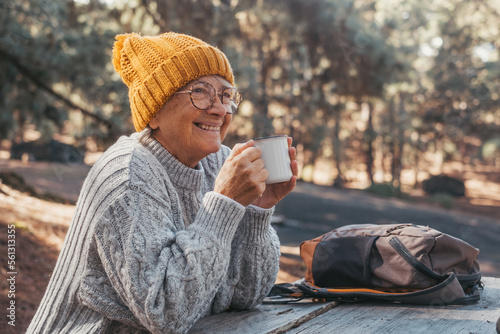 Head shot portrait close up of middle age woman relaxing drinking coffee or tea sitting at table in the forest of mountain in the middle of nature. Autumn season enjoying concept lifestyle. #561313355
