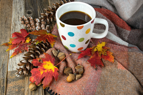 Polka dot coffee mug on a soft blanket with autumn leaves, acorns, and pine cones