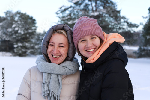 Concept of happy family, old age, emotions, walk in the winter forest of mom and adult daughter hugging outside. Woman smile. Around the green pine forest background of Christmas tree in forest.