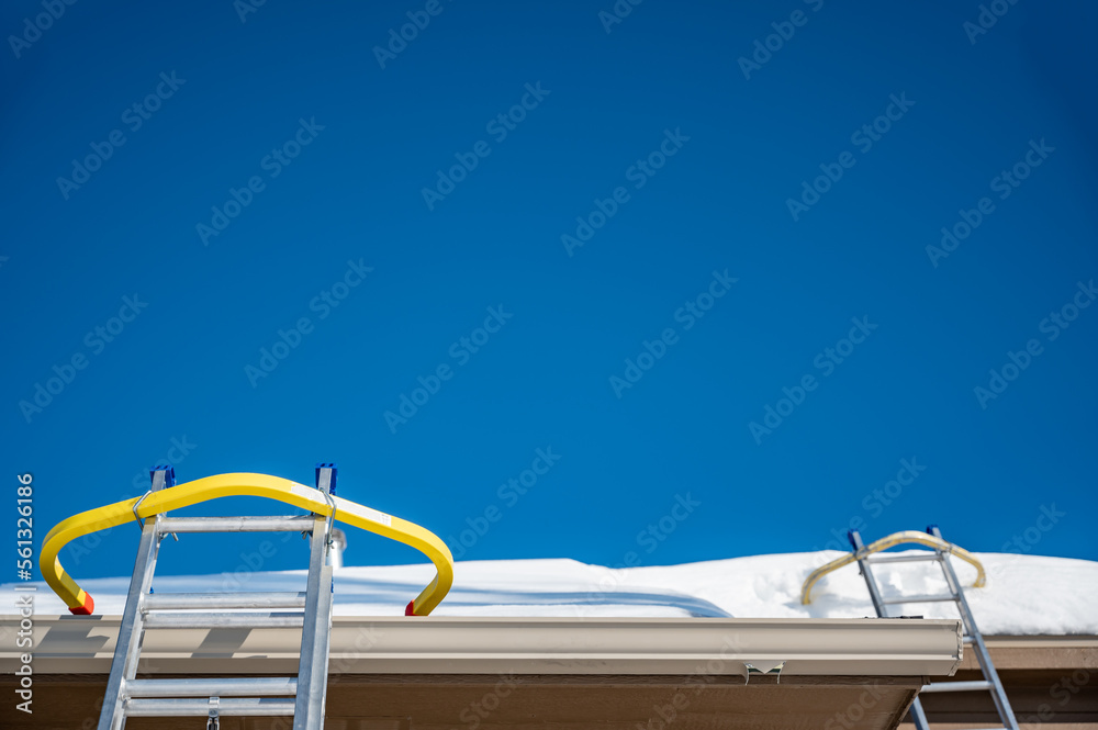 Naklejka premium Ladder and safety hook on a residential roof covered in snow as gutters are being installed. 