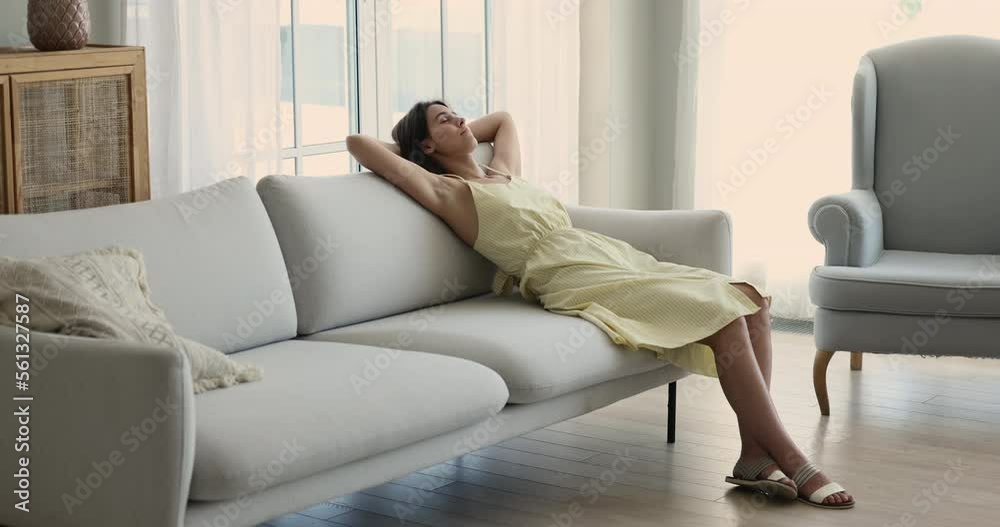 Young attractive woman in casual dress resting in living room alone, leaned on cozy couch, enjoy cool fresh air at sunny summer day at modern smart home, spend pleasant leisure on weekend. Relaxation Young attractive woman in casual dress resting in living room alone, leaned on cozy couch, enjoy cool fresh air at sunny summer day at modern smart home, spend pleasant leisure on weekend. Relaxation